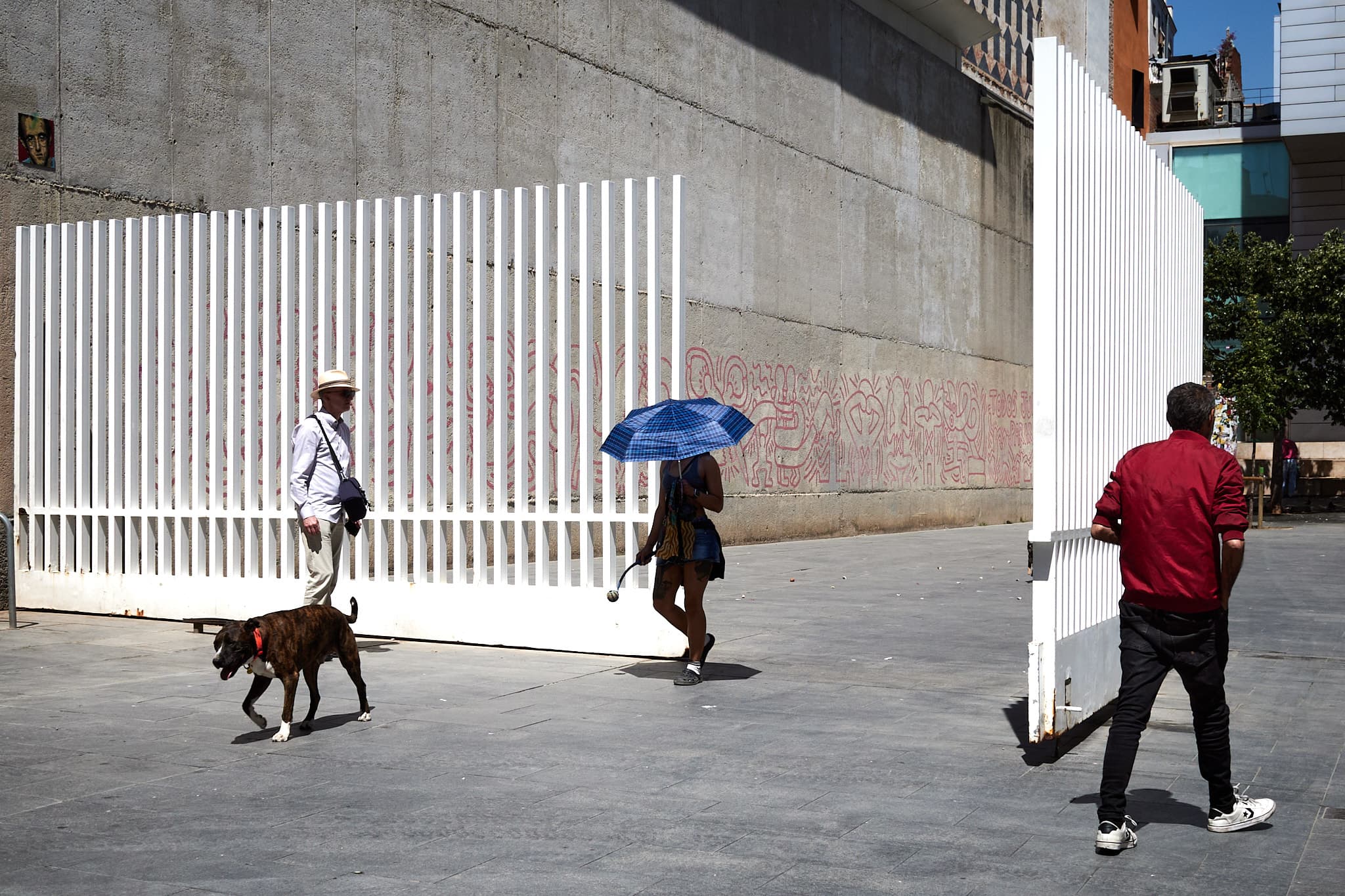 Pedestrians and a dog crossing between white gates in Barcelona